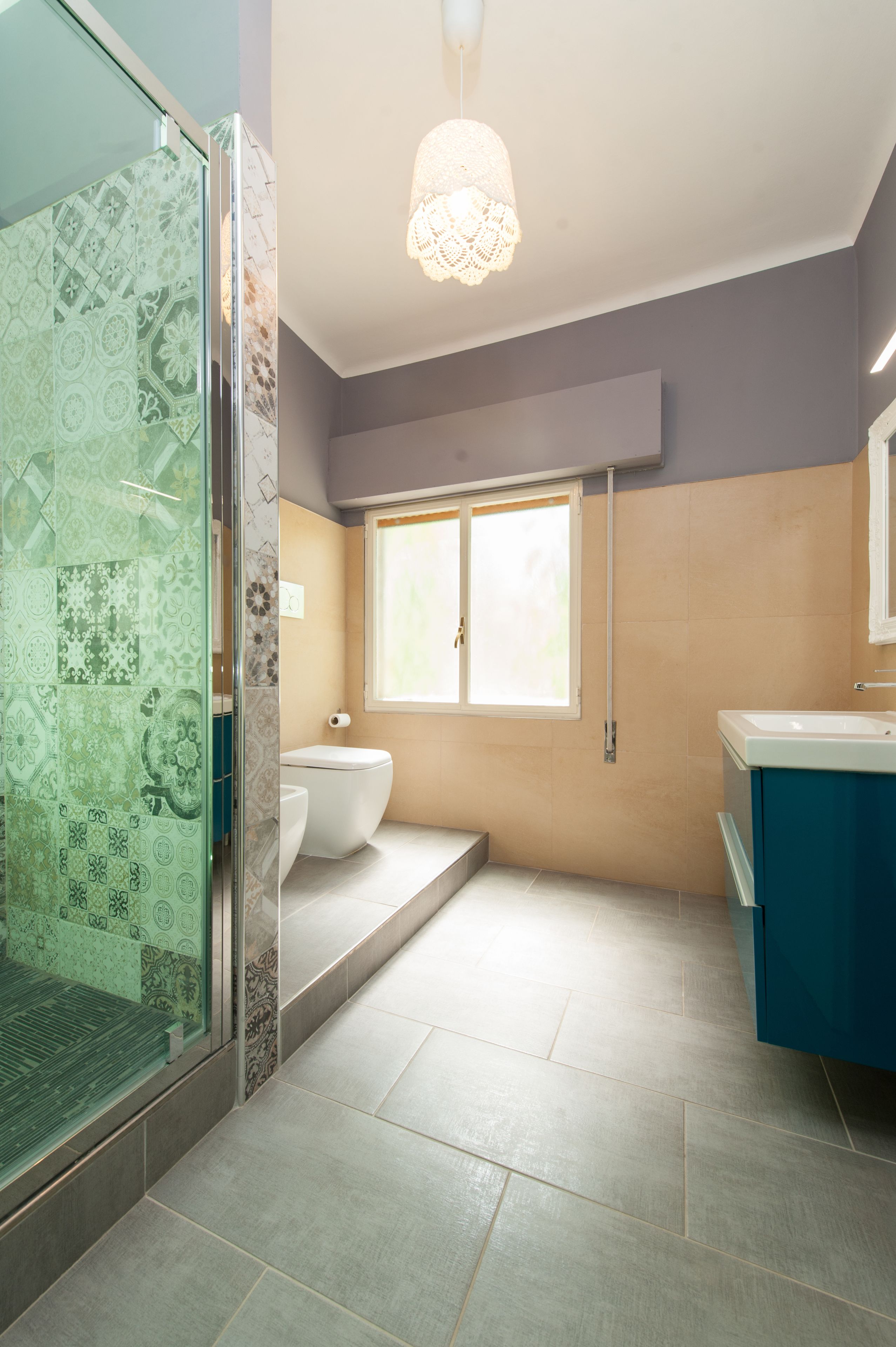 Une salle de bain dotée d’une douche à parois de verre, de toilettes, d’un lavabo et d’une fenêtre laissant entrer la lumière naturelle.