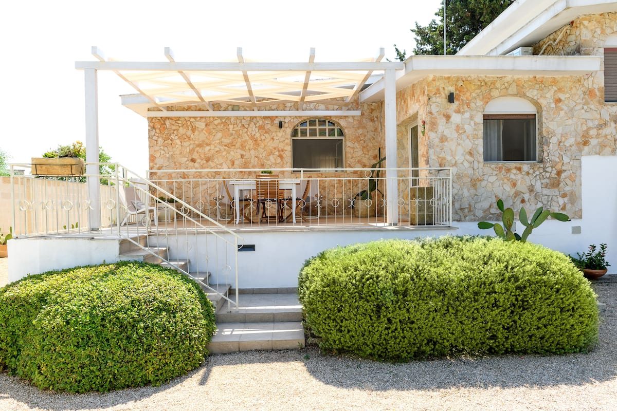 A modern house with a stone facade, a covered patio with outdoor furniture, and a well-maintained garden.