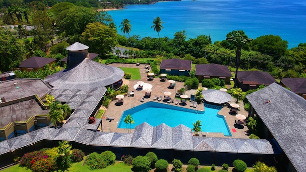 A resort with a swimming pool surrounded by lounge areas and umbrellas, overlooking a beach and ocean.