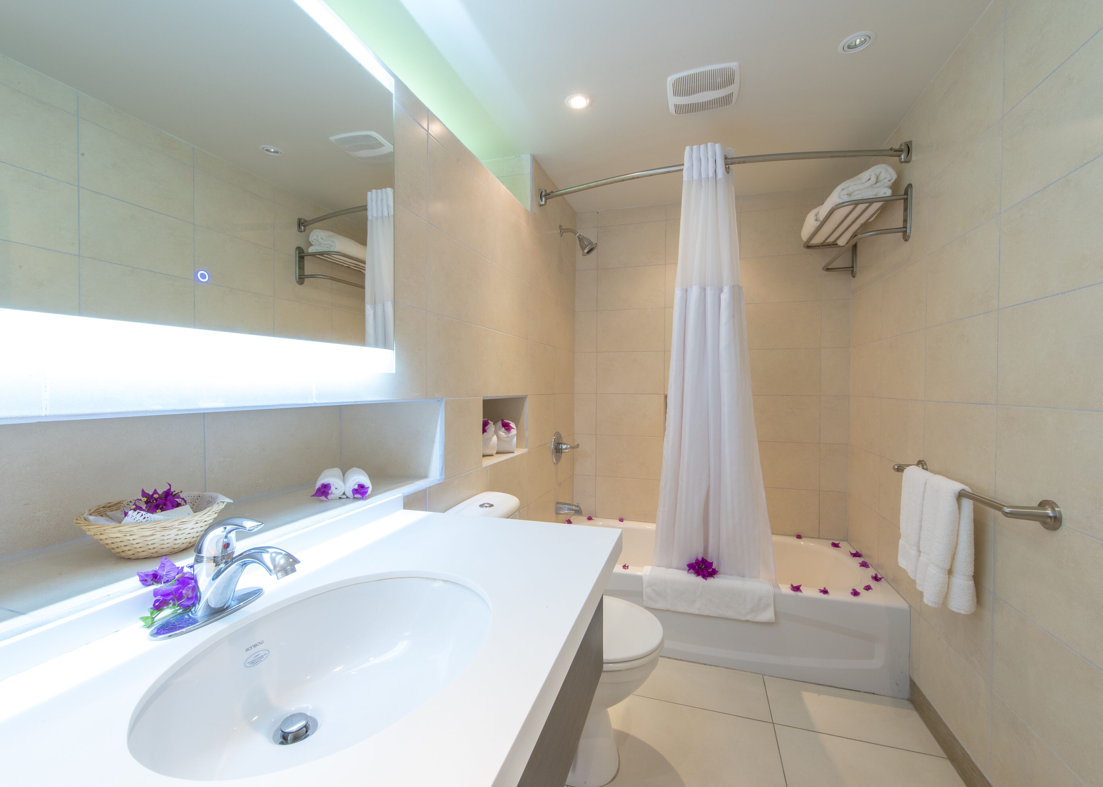 A modern bathroom with a white sink, toilet, and bathtub. There are shelves with towels and a shower curtain.