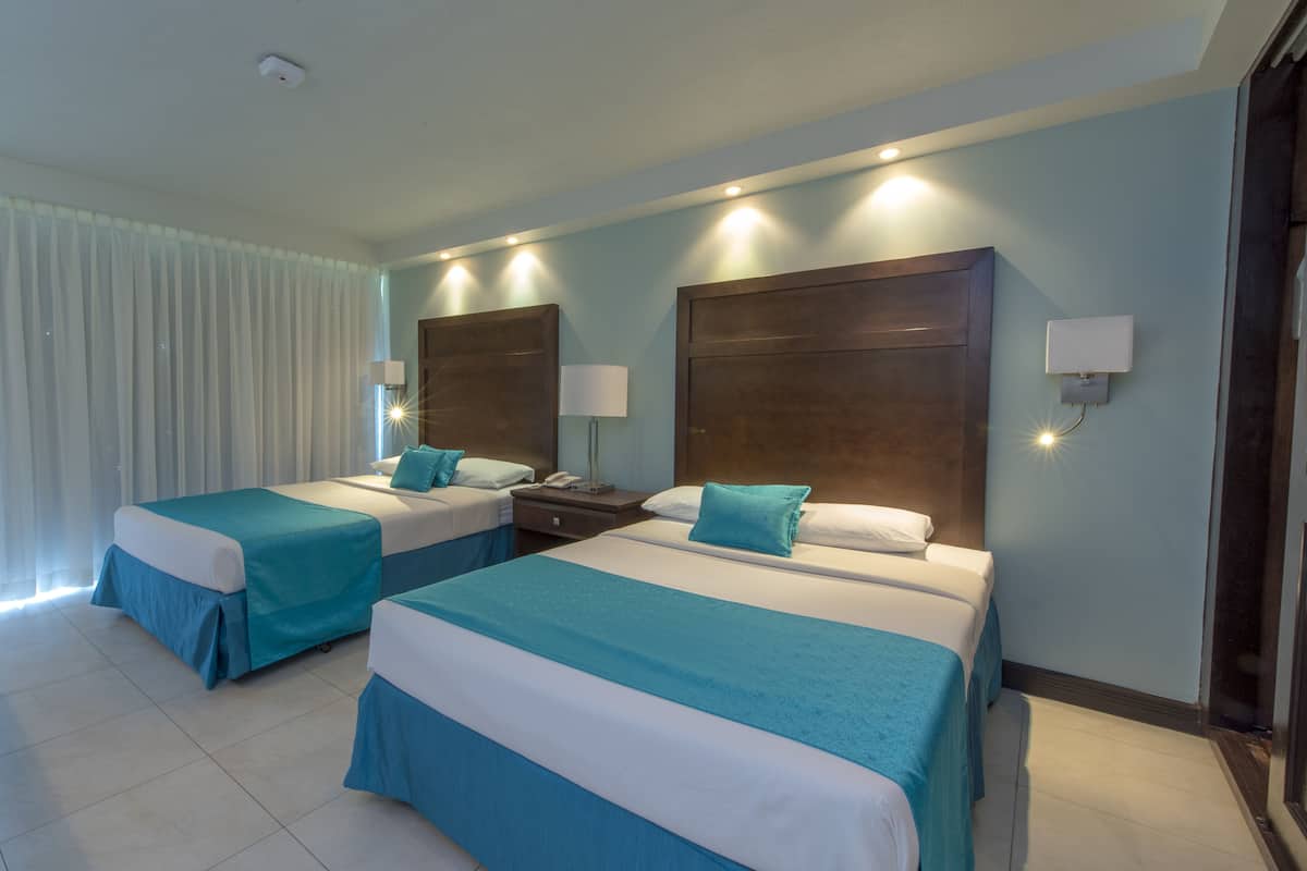 A hotel room with two beds, each with a blue and white bedspread, a wooden headboard, and a nightstand with a lamp.
