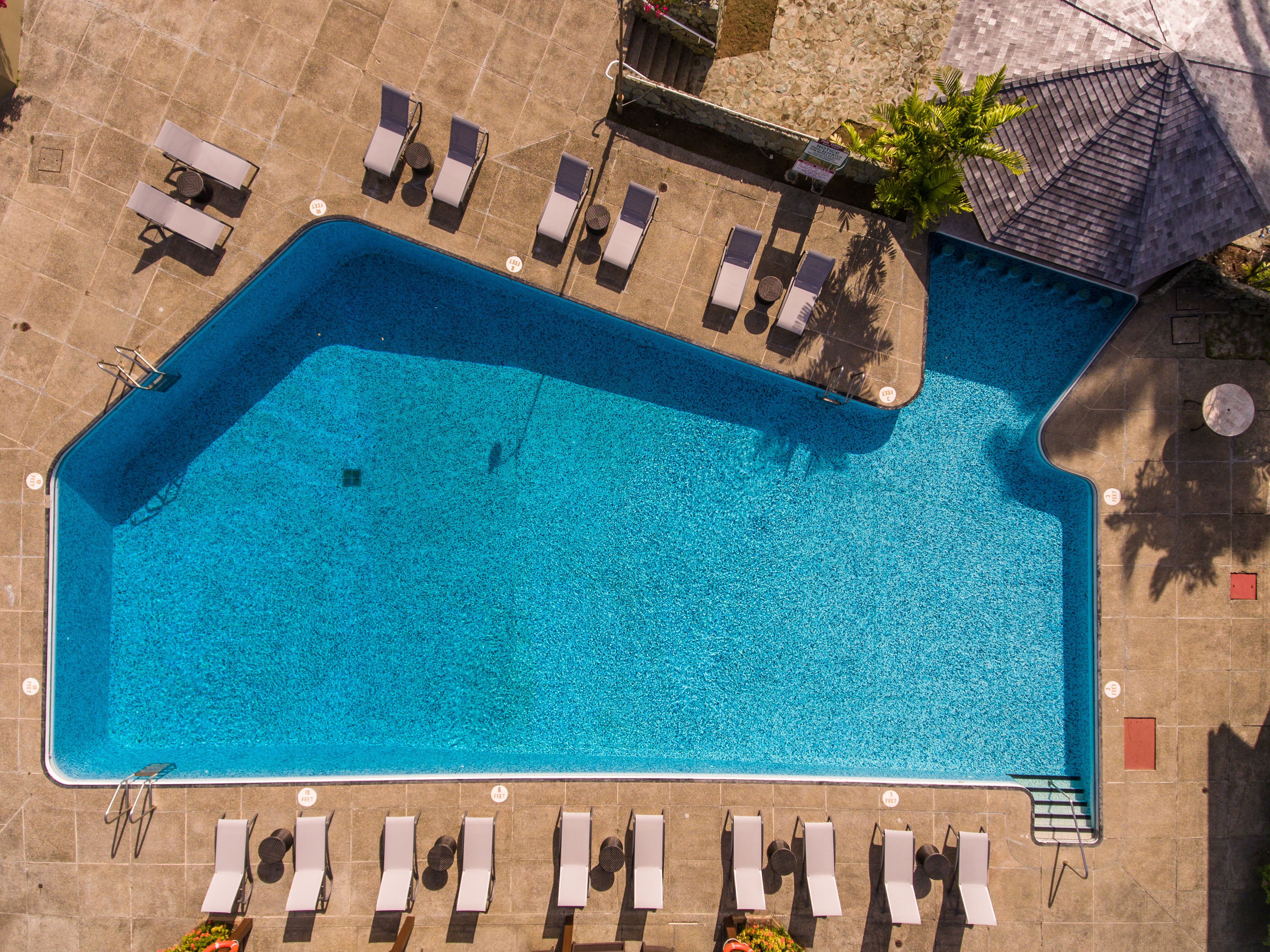 An aerial view of a rectangular swimming pool with multiple lounge chairs and umbrellas around the perimeter.