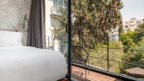 Een slaapkamer met een groot bed, uitzicht op een balkon met een metalen hekwerk, en een stadsbeeld op de achtergrond.