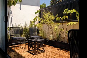 Un patio con dos sillas de metal negro y una mesa, rodeado de plantas en macetas y un suelo de madera.