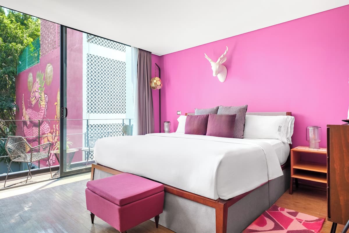 A modern hotel room with a large bed, pink walls, and a balcony with a decorative mural.