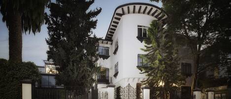 A modern building with a curved facade, large windows, and a gated entrance surrounded by trees.