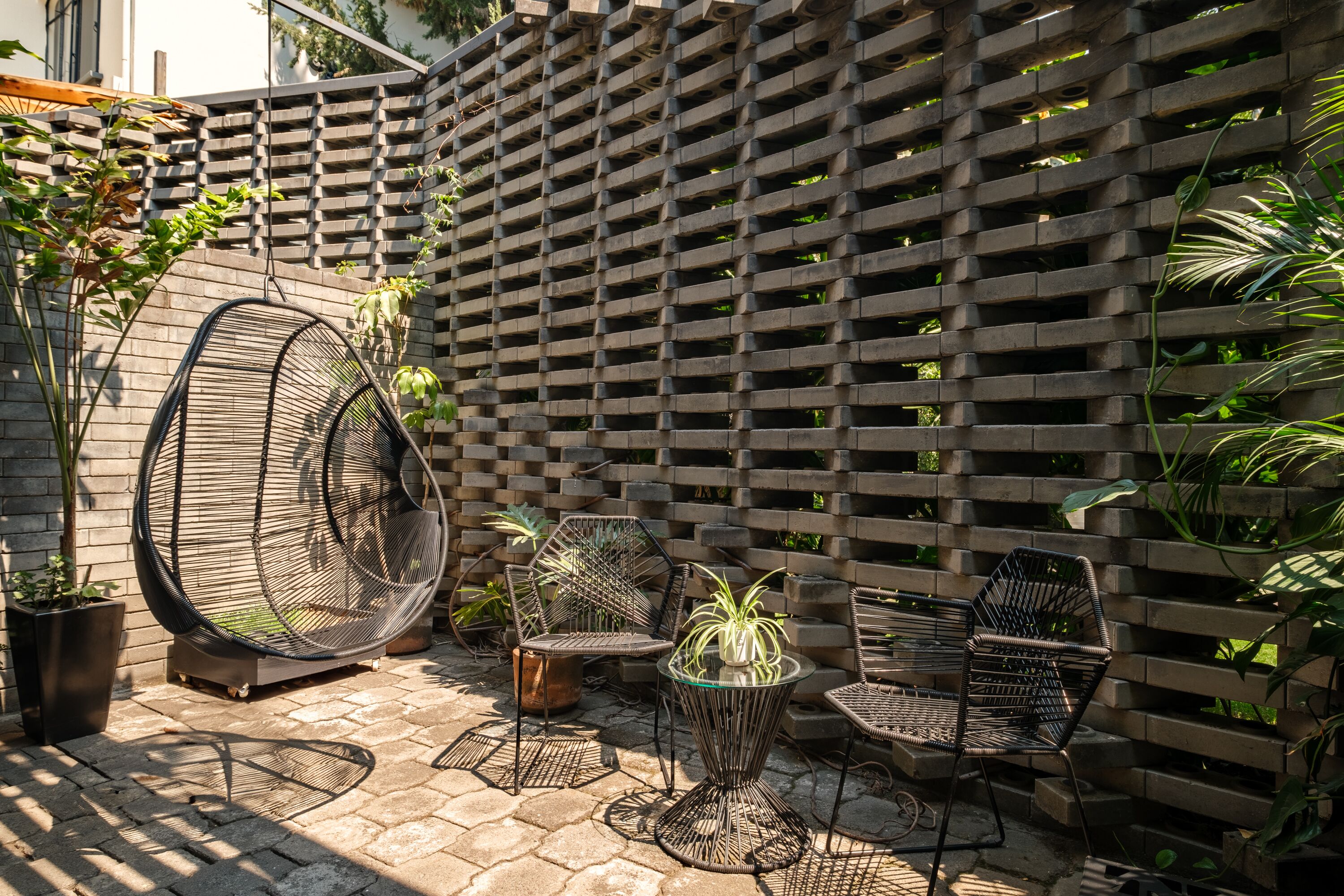 A patio area with a hanging chair, two chairs, a small table, and potted plants.