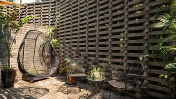 A patio area with a hanging chair, two chairs, a small table, and potted plants.