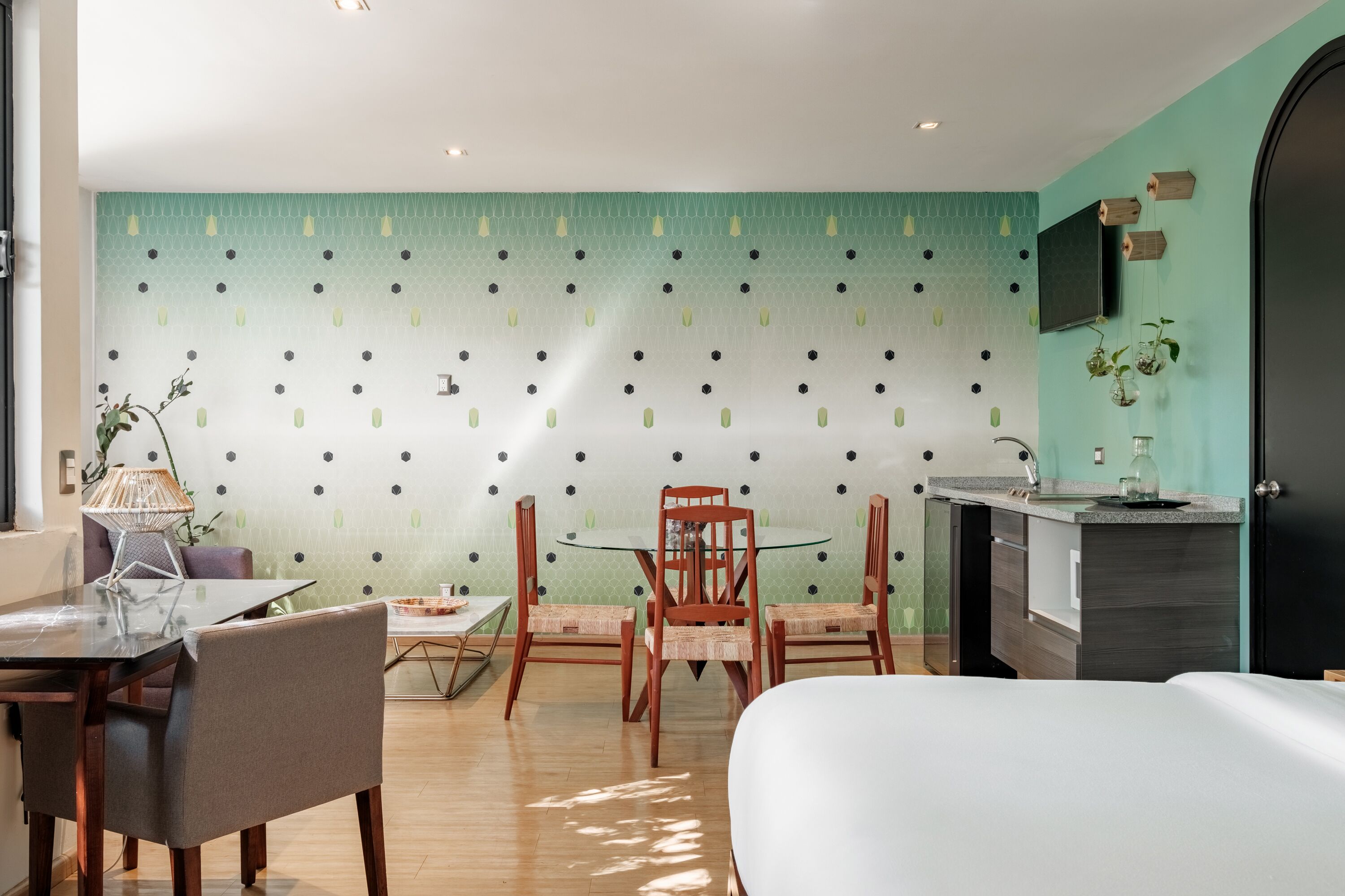 Habitación de hotel moderna con zona de comedor, televisor montado en la pared y una pequeña encimera de cocina.