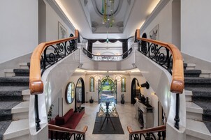 Una imponente escalera con barandilla de madera que conduce a un amplio vestíbulo con una instalación artística central.