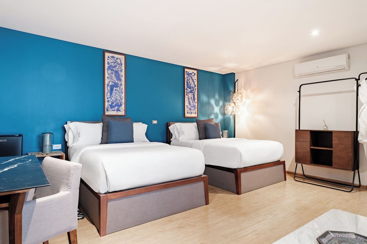 A hotel room with two beds, a desk, and a chair. There is a wardrobe and a mirror on the wall.
