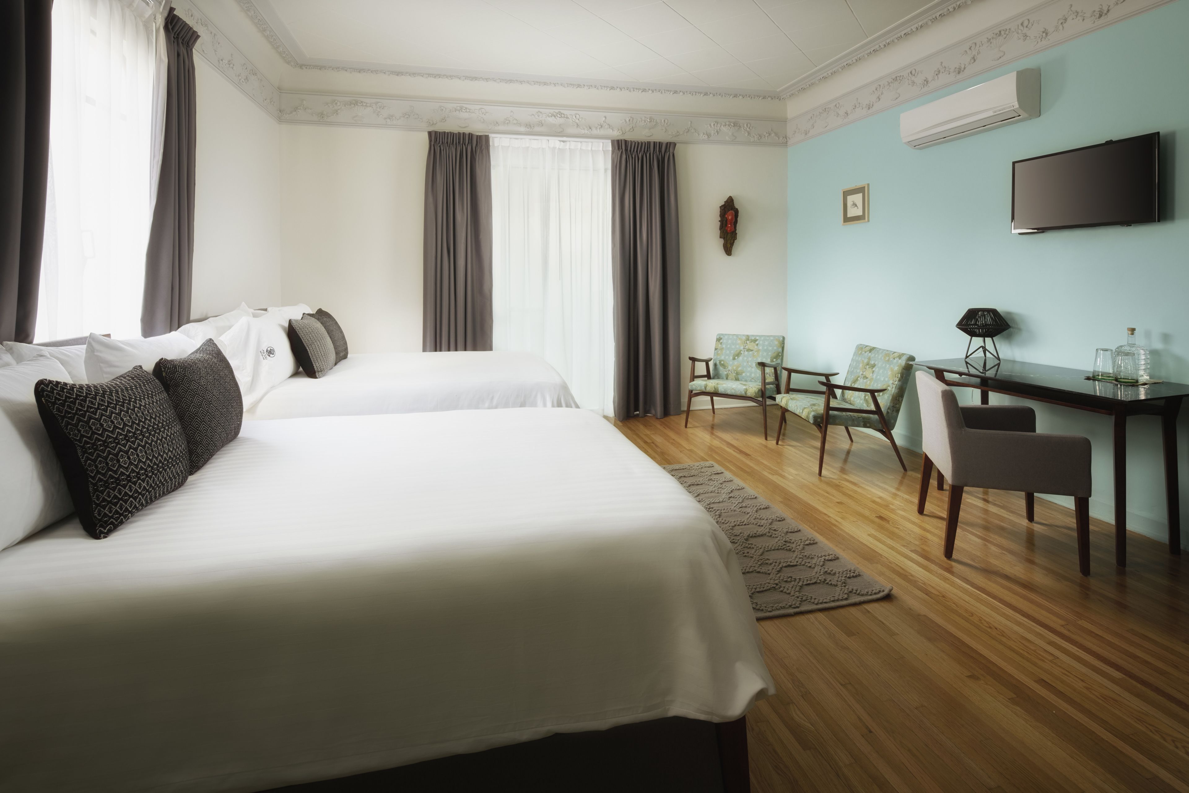 A hotel room with two beds, a desk, a chair, and a TV.