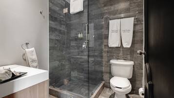 A modern bathroom with a glass-enclosed shower, a white toilet, and a vanity with a towel rack.