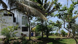 A white building with a sloped roof, surrounded by lush greenery and trees. - Villa Madeleine (Micoud)