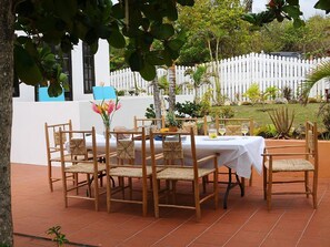 An outdoor dining area with a white table and chairs, surrounded by a white fence and greenery. - Villa Madeleine (Micoud)