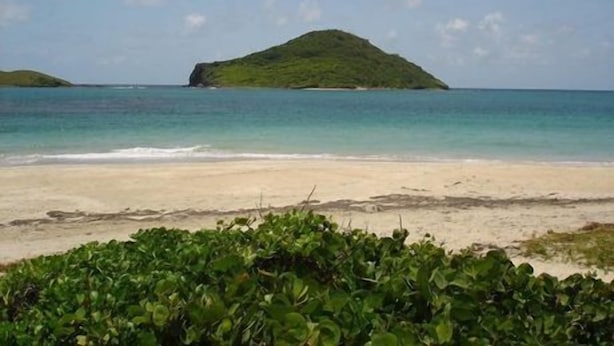 A beach with clear turquoise water, a sandy shore, and a small green island in the distance. - Villa Madeleine (Micoud)