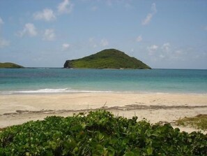 A beach with clear turquoise water, a sandy shore, and a small green island in the distance. - Villa Madeleine (Micoud)