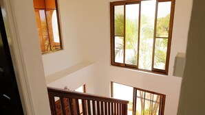A multi-level interior with a wooden staircase, large windows with a view of greenery, and a white wall. - Villa Madeleine (Micoud)