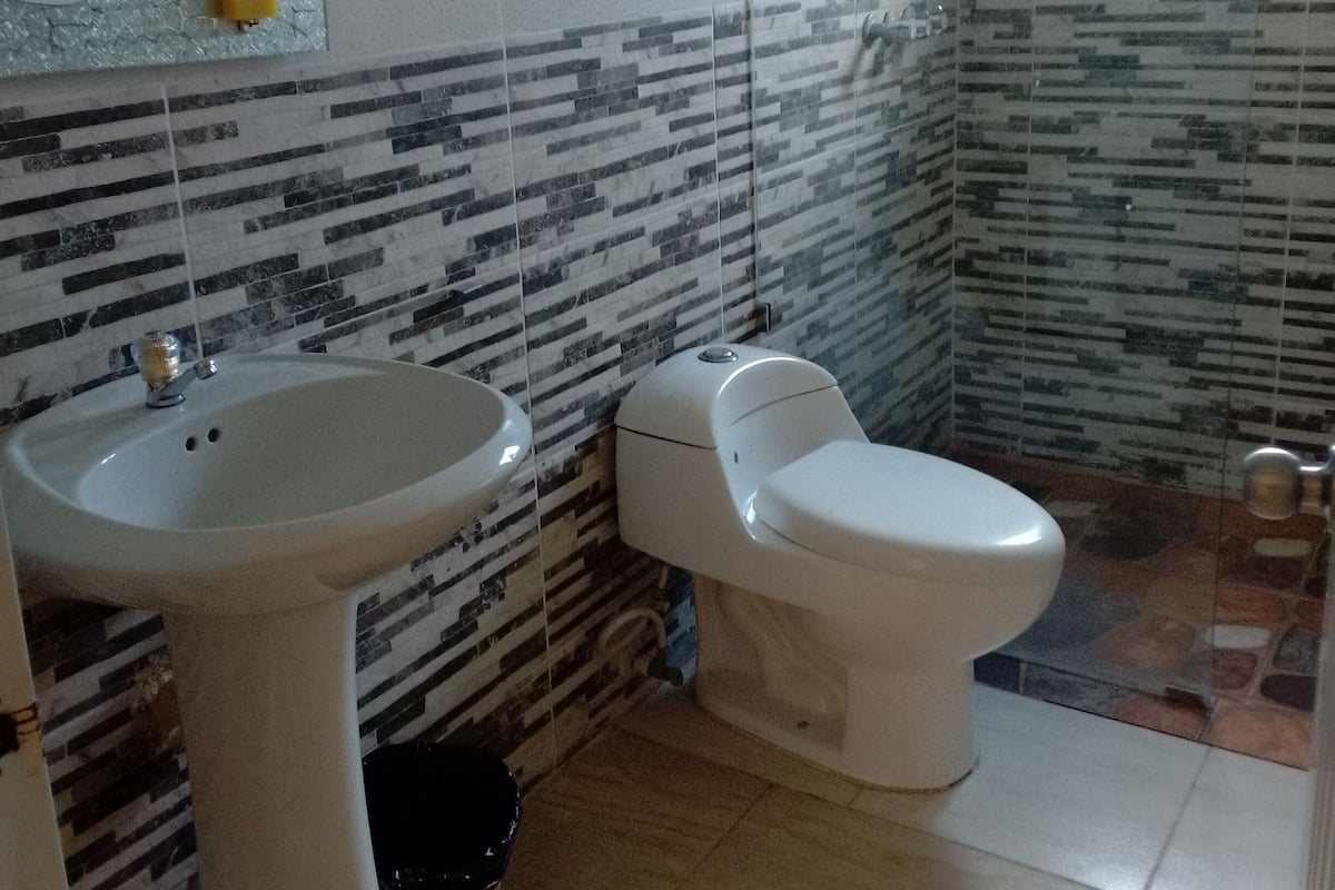 A bathroom with a sink, toilet, and shower. The walls have a patterned tile design.