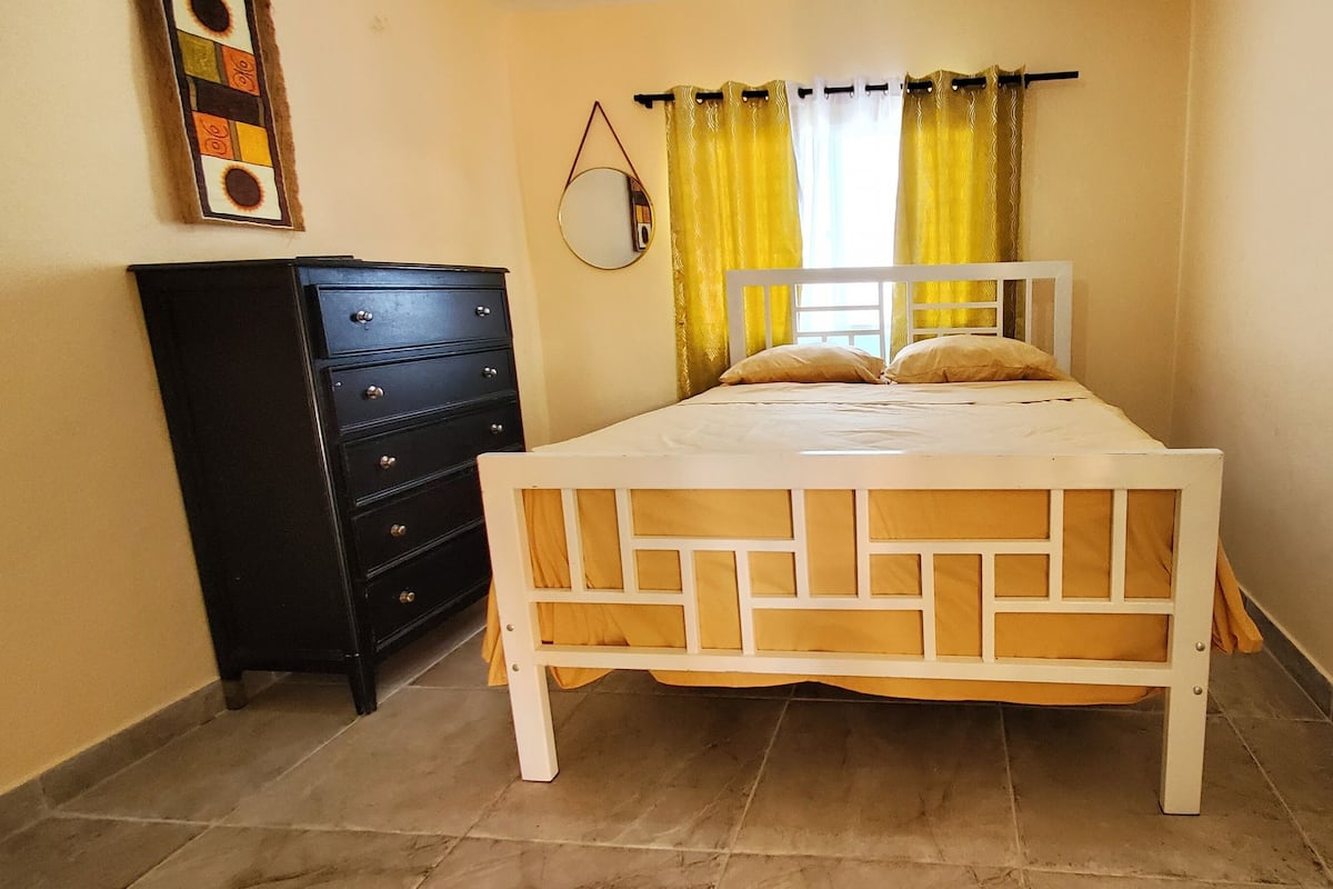 A bedroom with a bed, a dresser, a mirror, and curtains.