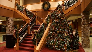 Un magnifique escalier, avec un grand sapin de Noël décoré de guirlandes lumineuses et d’ornements, flanqué de rampes en bois et de piliers en pierre.
