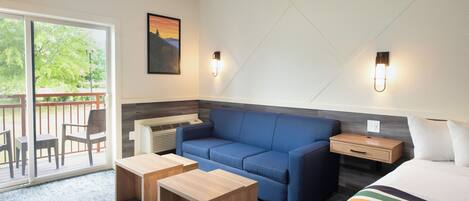 A modern hotel room with a blue sofa, a wooden nightstand, a small table, and a bed with a striped blanket.