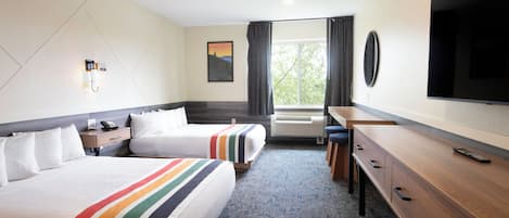 A hotel room with two beds, a desk, a TV, and a window with curtains.
