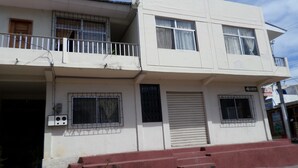 A two-story building with a balcony on the upper floor, a closed shutter on the ground floor, and a visible electrical box. - Hostal Miconia (Puerto Ayora)