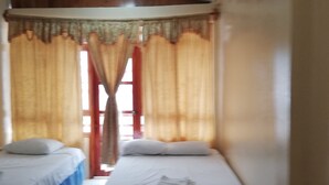 A room with two single beds, a wooden headboard, a small table, and a window with curtains. - Hostal Miconia (Puerto Ayora)