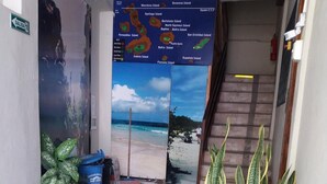 A hallway with a map of Galápagos Islands, potted plants, and a beach scene. - Hostal Miconia (Puerto Ayora)