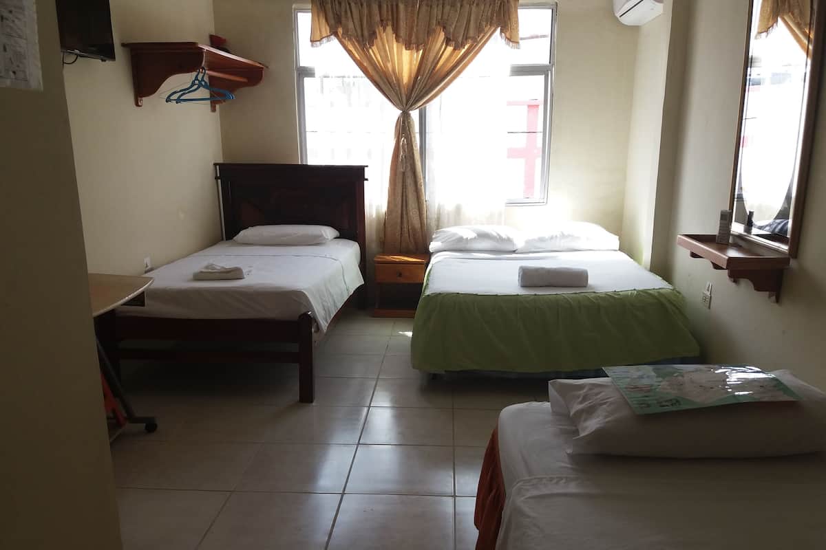 Une chambre d’hôtel avec deux lits simples, une petite table, une chaise, un téléviseur et une fenêtre avec des rideaux.