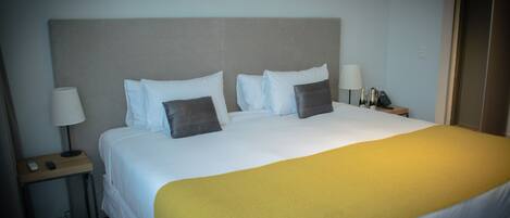 A hotel room with a large bed, white bedding, a grey headboard, two bedside tables with lamps, and a yellow throw blanket.