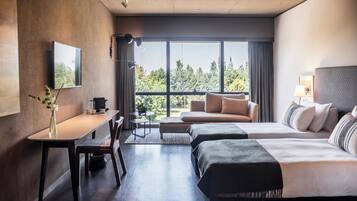Una habitación de hotel moderna con un ventanal grande, un sofá, una cama, un escritorio y un televisor.