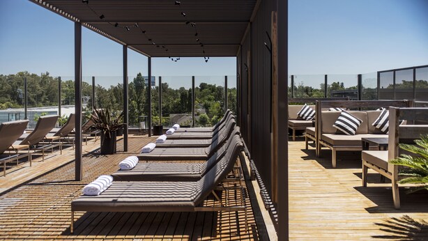 A wooden deck with lounge chairs and a covered seating area, overlooking a body of water and greenery. - Kos Pilar Hotel (Villa Rosa)