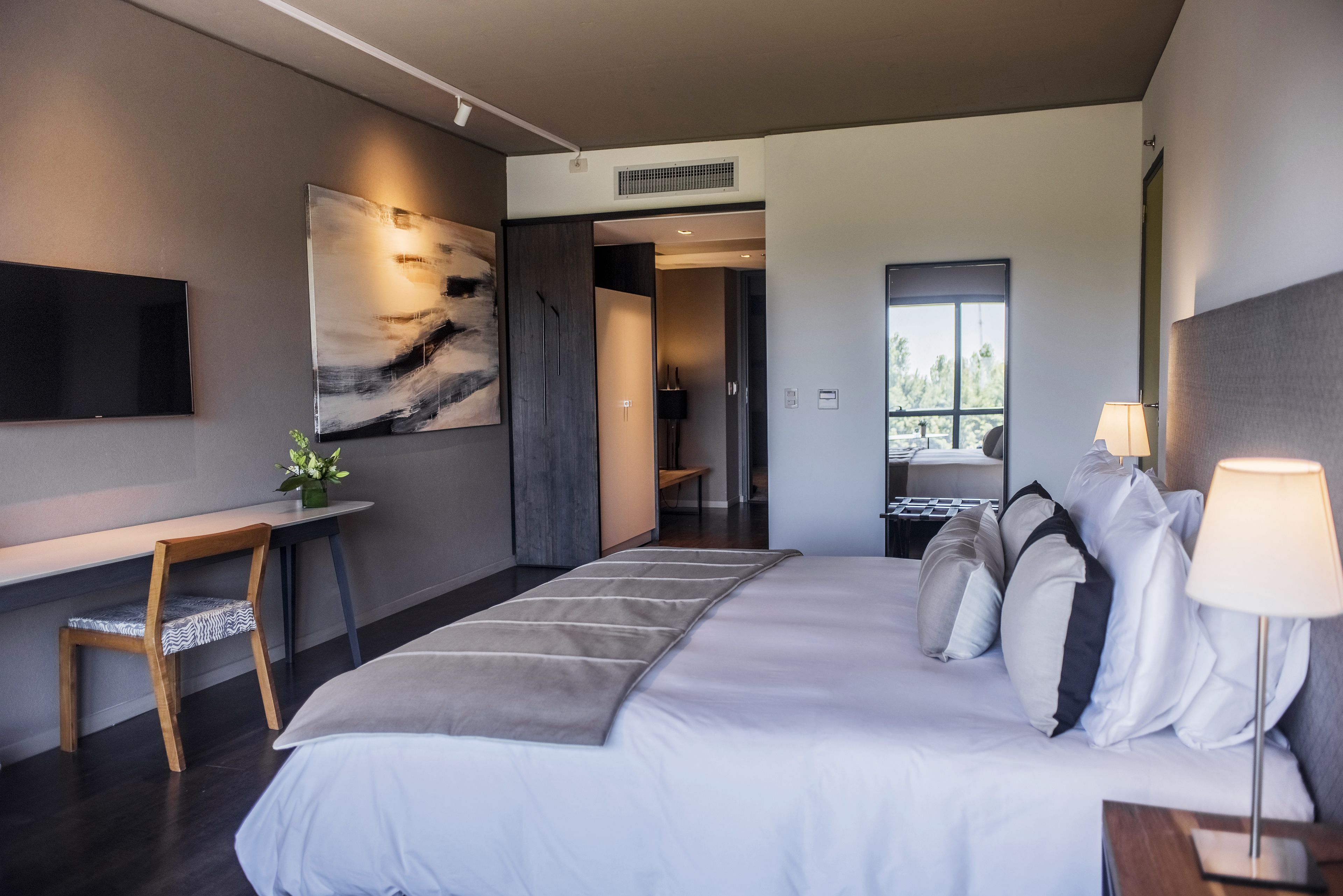 Una habitación de hotel moderna con una cama grande, un escritorio con silla, un televisor de pantalla plana y un cuadro abstracto de gran tamaño en la pared.