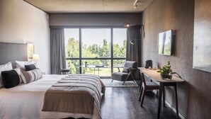 A modern hotel room with a large bed, a desk, and a view of the outdoors through a large window. - Kos Pilar Hotel (Villa Rosa)