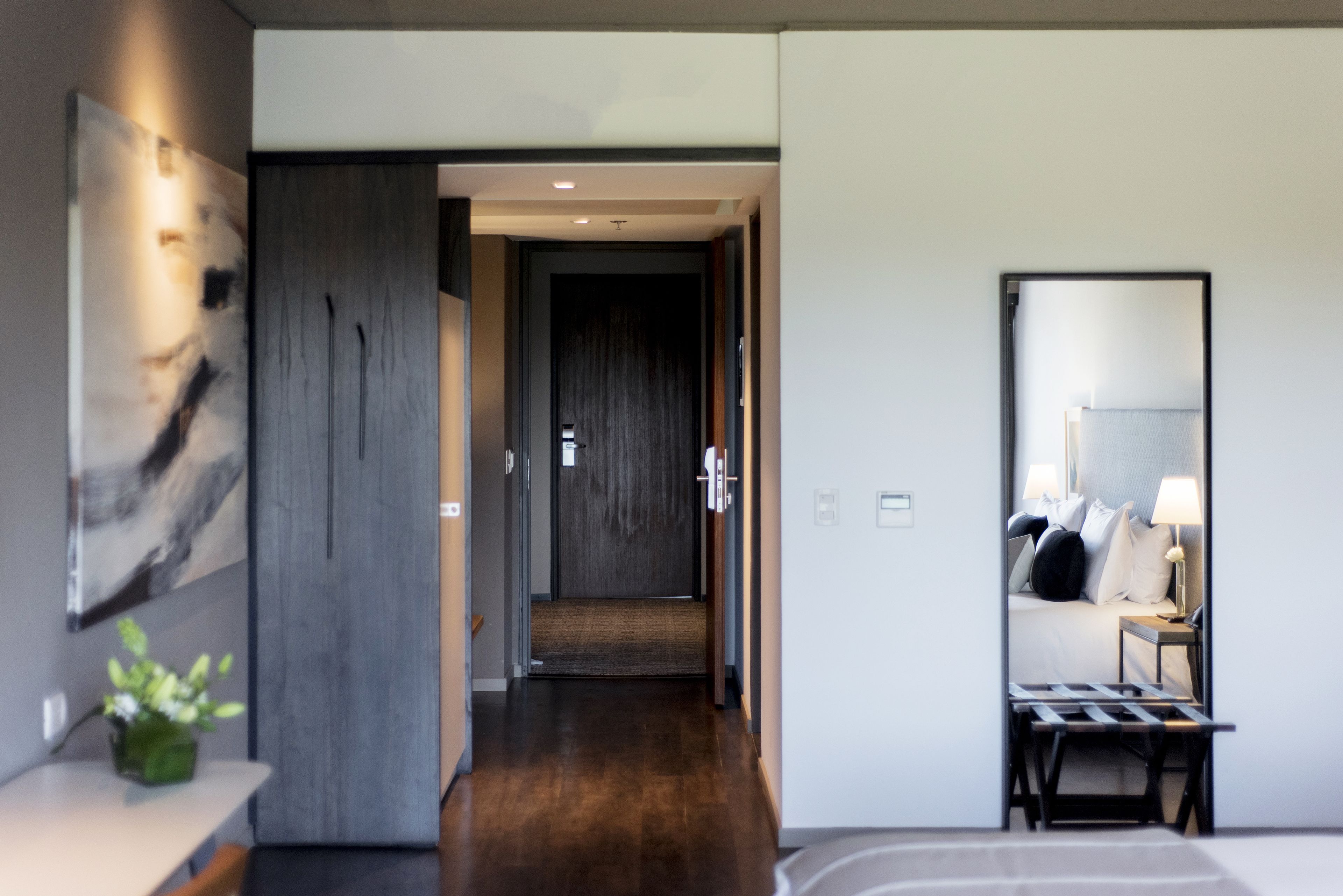 Een moderne hotelkamer met een houten vloer, een bed met nachtkastje, een spiegel en een kunstwerk aan de muur.