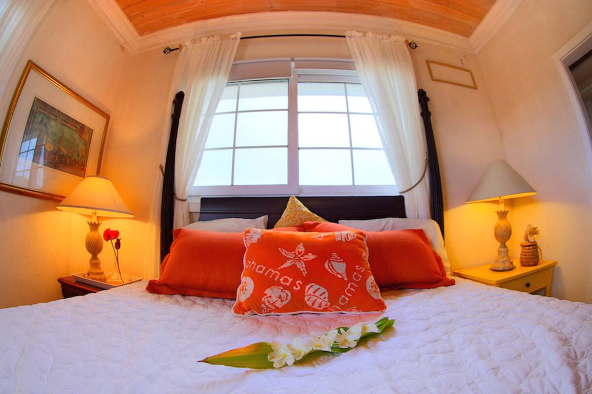 A hotel room with a large bed, two nightstands, a window with curtains, and a framed picture on the wall.