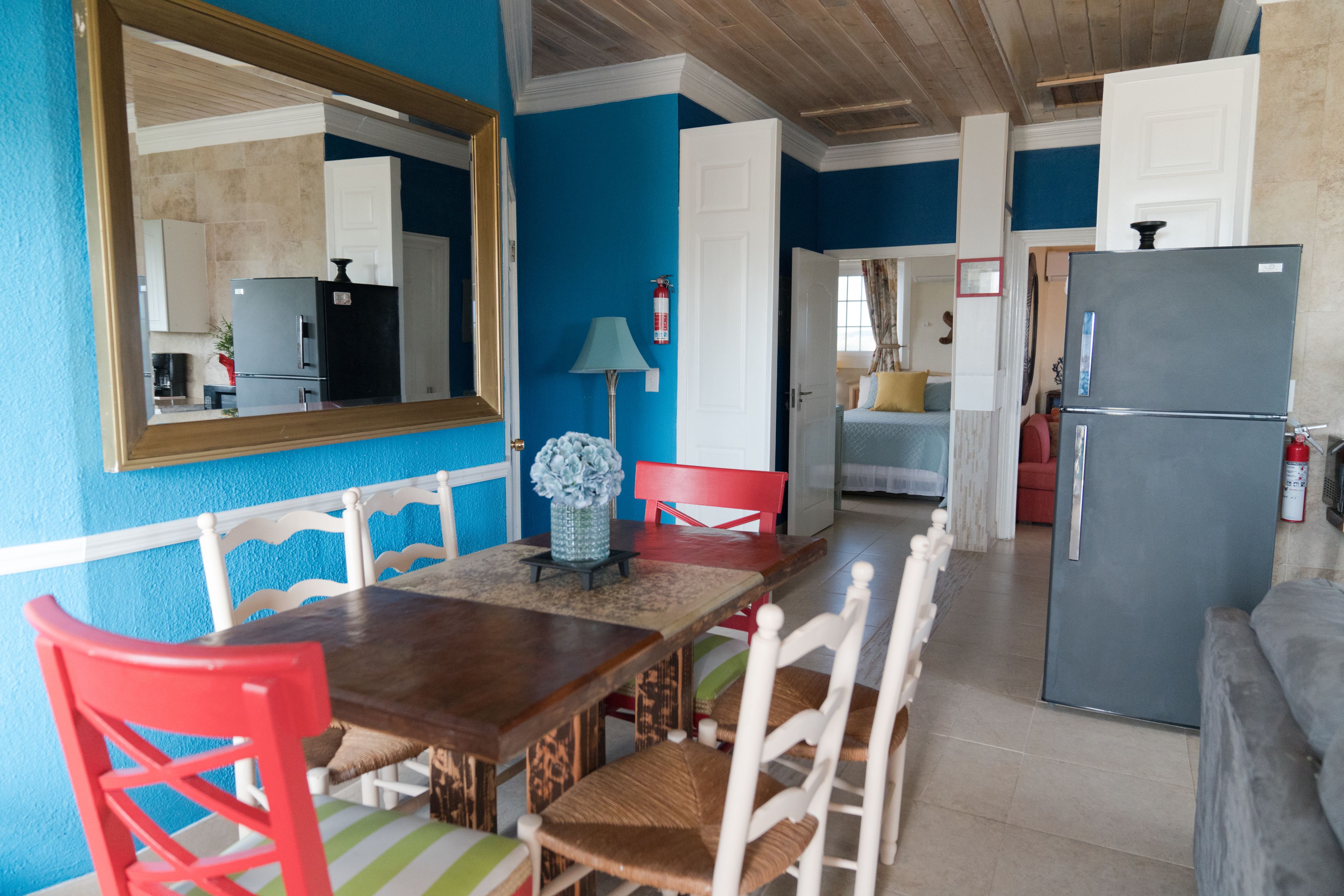 A dining area with a wooden table, red and white chairs, a vase with flowers, and a large mirror on the wall.