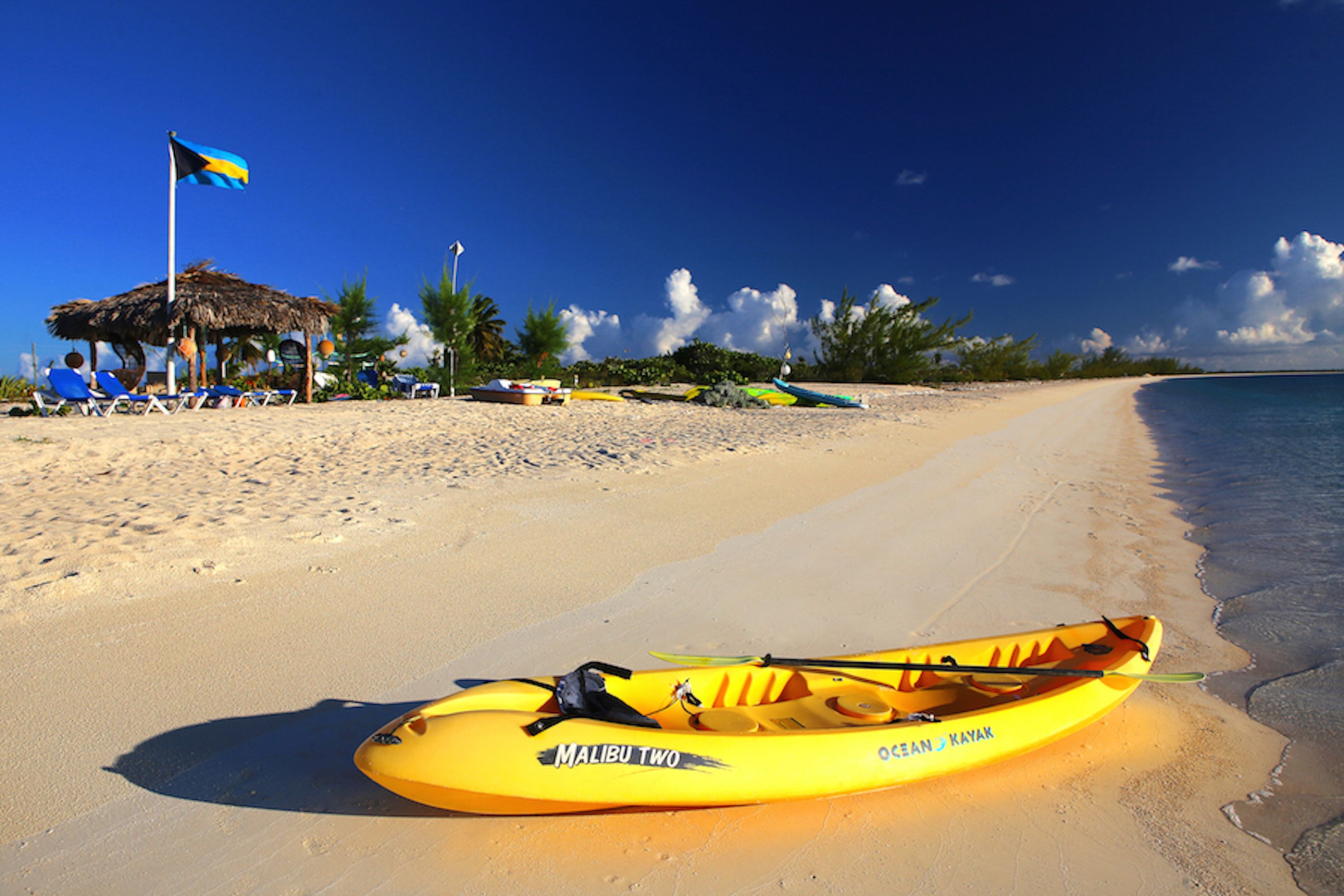 A beach with a yellow kayak labeled "Malibu Two" and a flag.