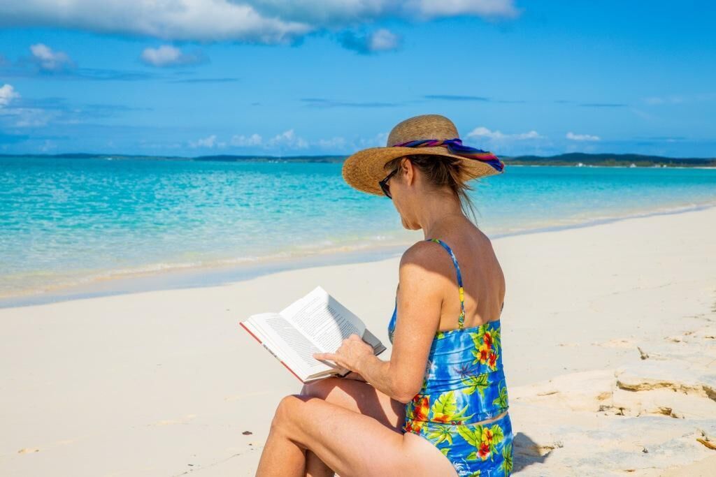 Una persona sentada en la playa leyendo un libro.