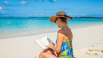 Una persona sentada en la playa leyendo un libro.