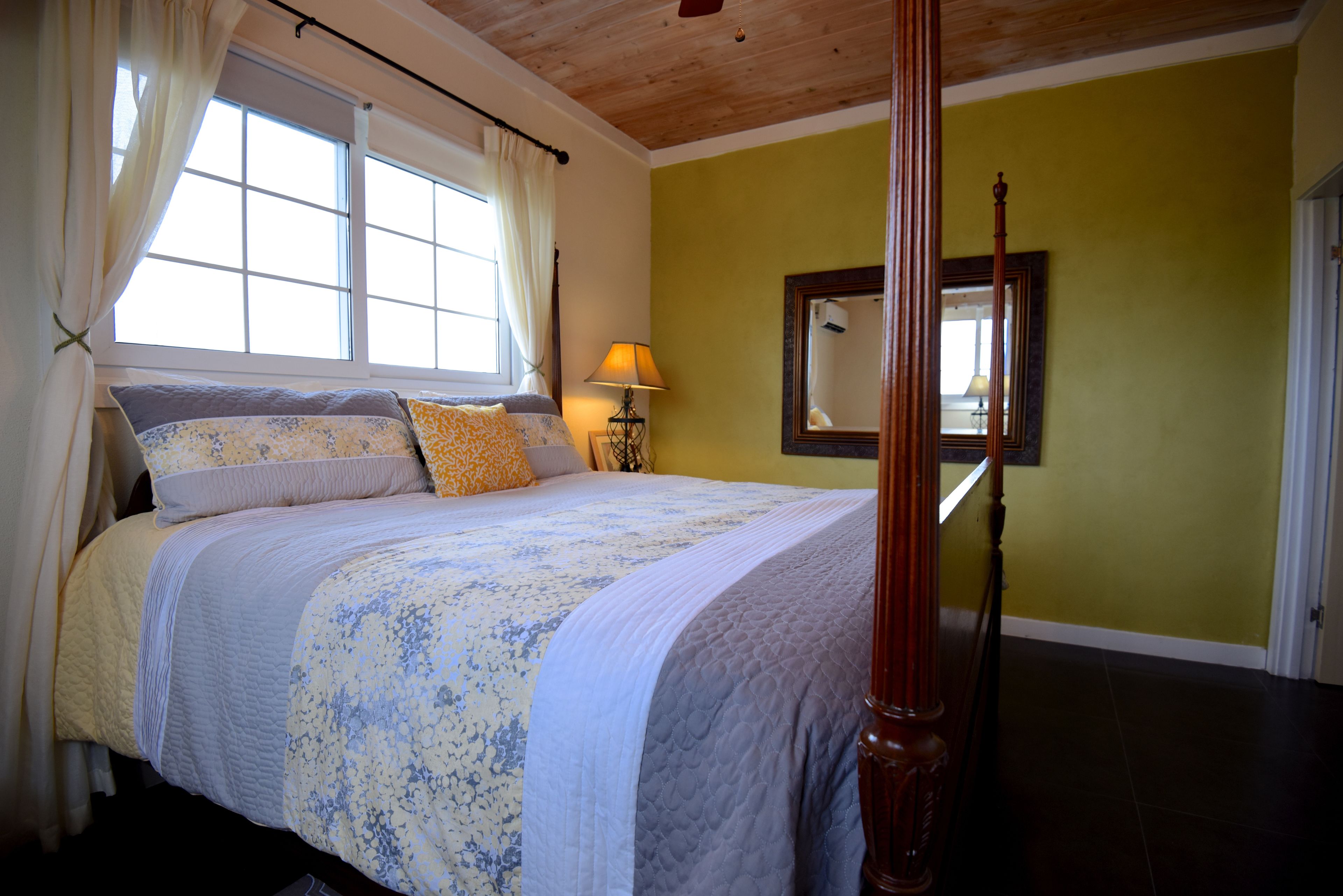 A four-poster bed with a floral bedspread, a bedside lamp, and a mirror on the wall.