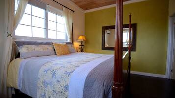 A four-poster bed with a floral bedspread, a bedside lamp, and a mirror on the wall.