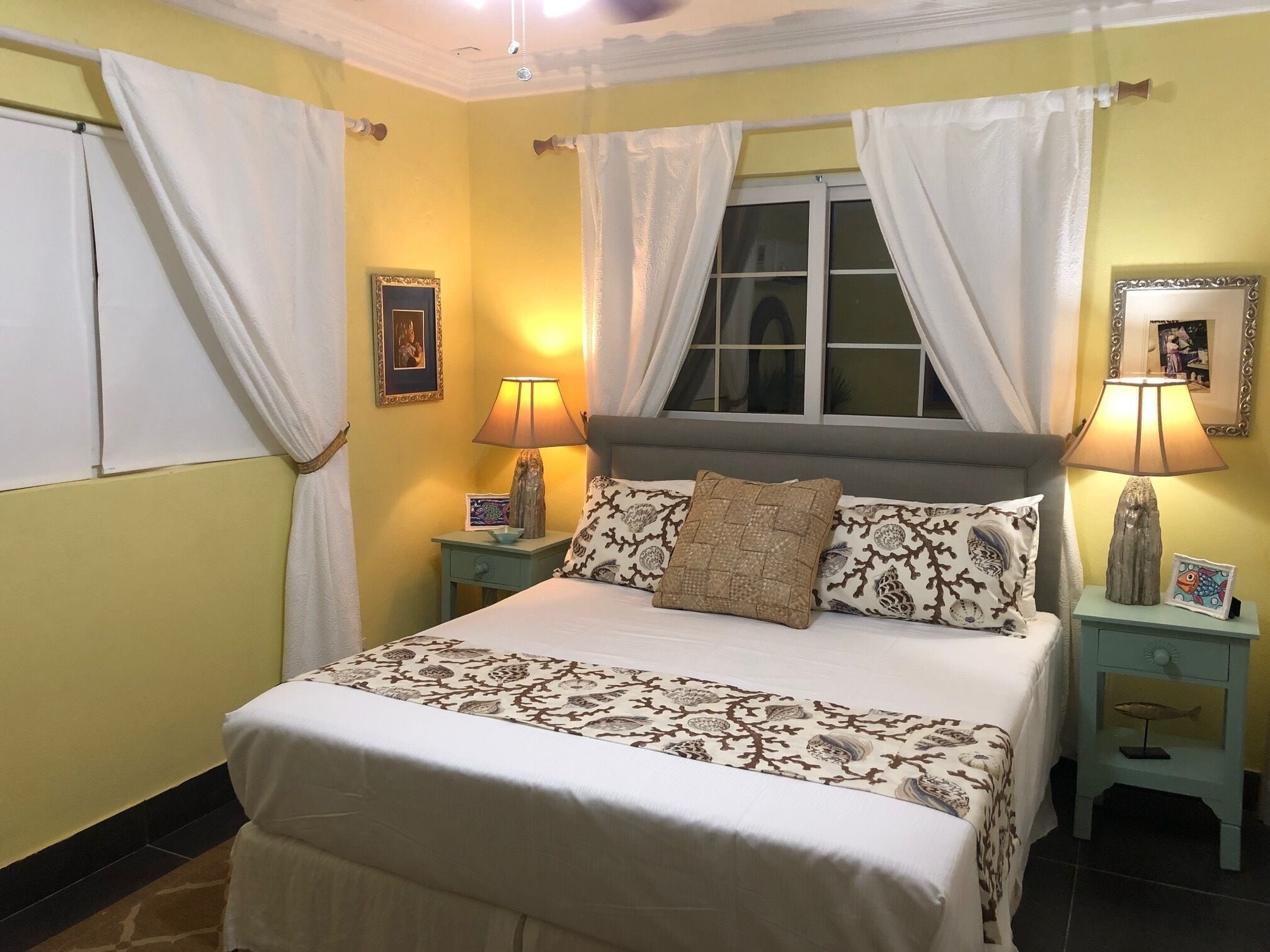 A neatly arranged bedroom with a bed, two bedside tables, a window with curtains, and a wall-mounted lamp.
