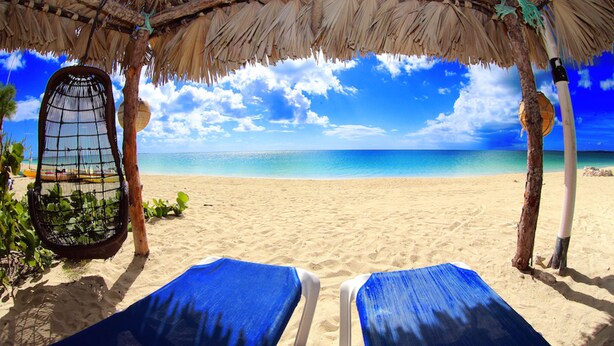 A beach with two blue lounge chairs under a thatched roof structure. - Rollezz Villas Beach Resort (Old Bight)
