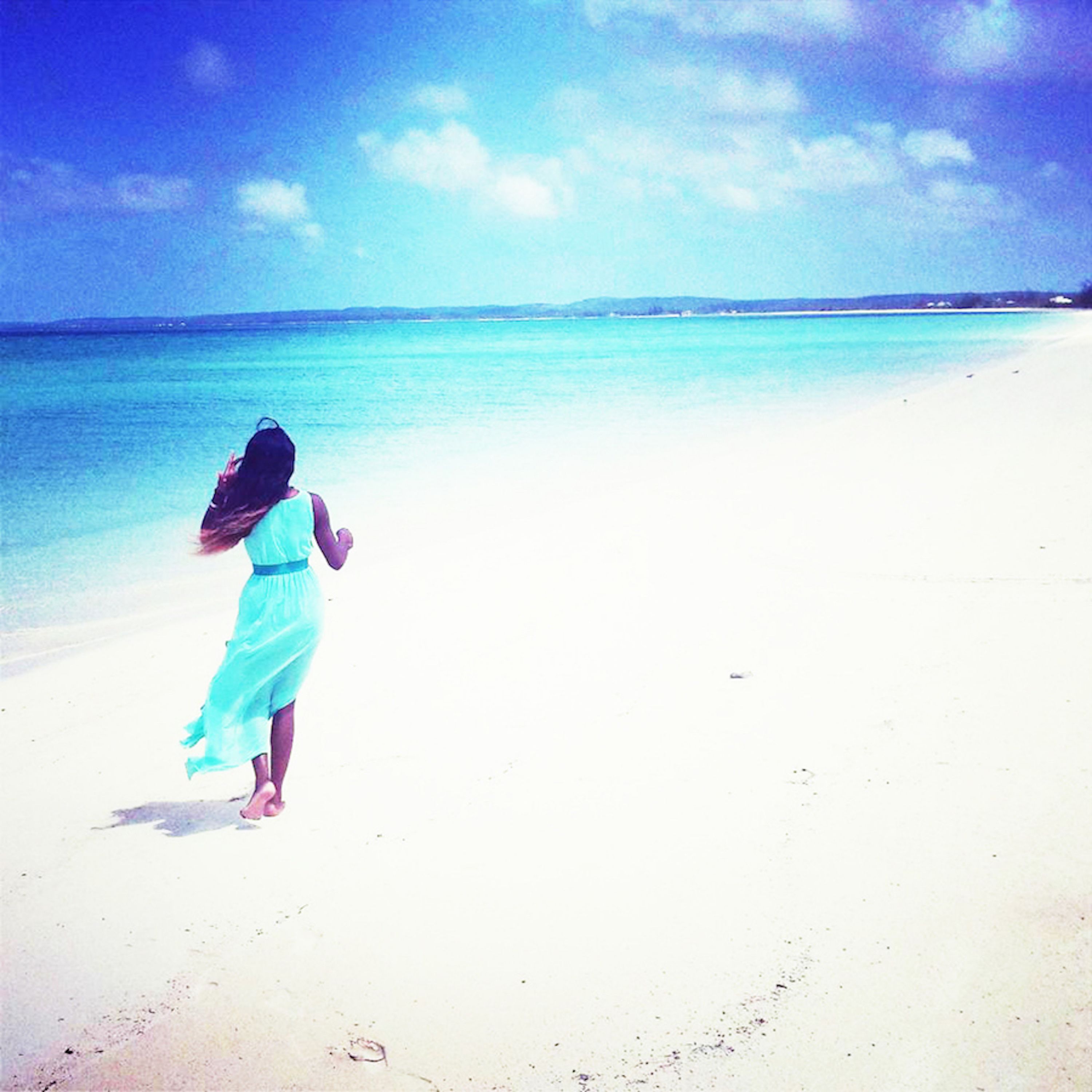 Escena de playa con una persona corriendo hacia el agua con un vestido azul claro.