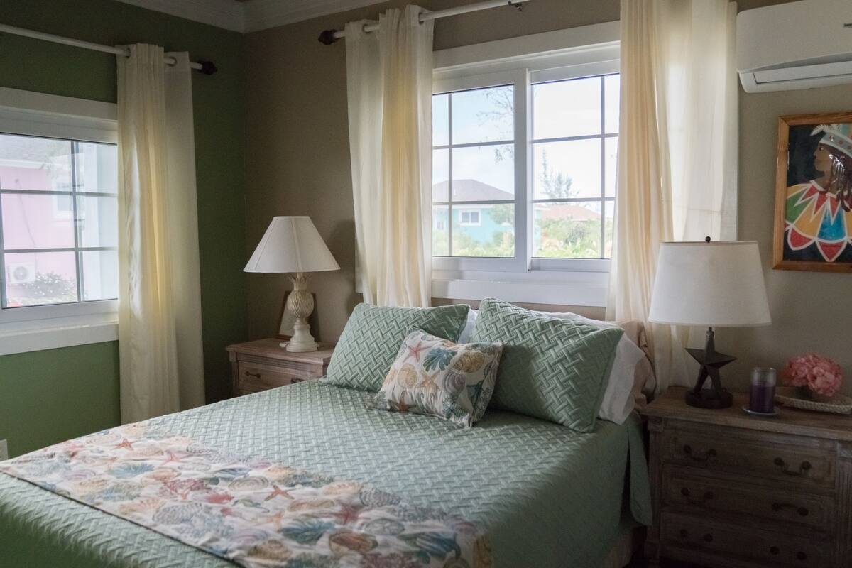 A bedroom with a bed, two bedside tables, a window, and a painting on the wall.
