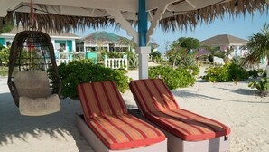 Two sun loungers with striped cushions under a thatched roof structure. - Rollezz Villas Beach Resort (Old Bight)
