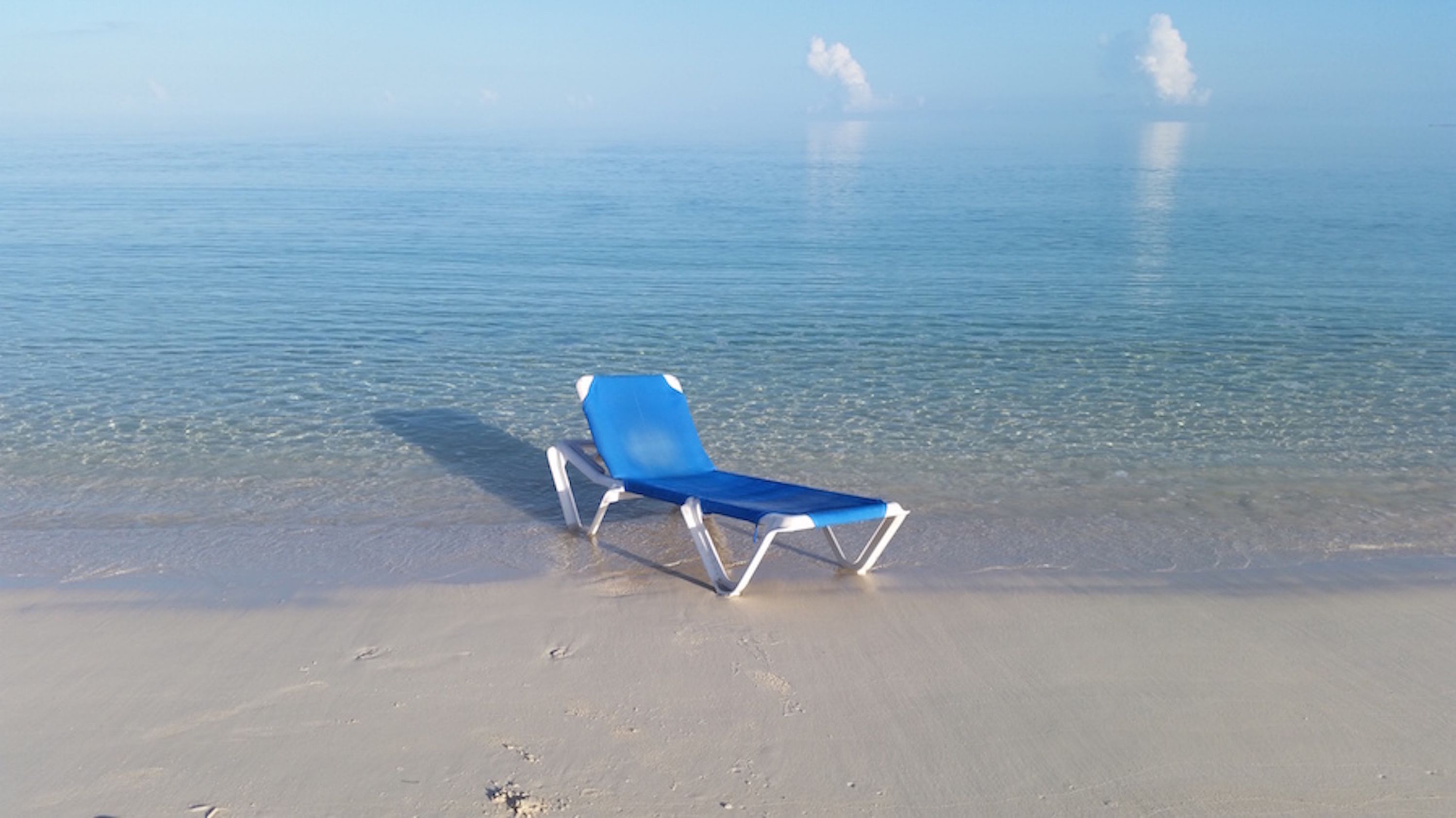 A beach with a single blue lounge chair on the sand.